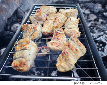 Grilled Meat Cooking Outdoors on a Barbecue open Fire in a Rustic Setting Grilled Meat Cooking Outdoors on a Barbecue open Fire in a Rustic Setting 129762520