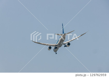 澄んだ青空の下を飛ぶ旅客機 129762959