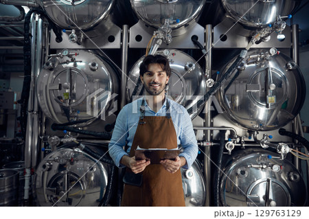 A man wearing an apron is holding a tablet inside a brewery facility 129763129