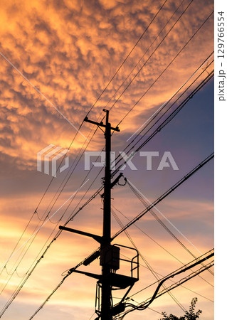 住宅街の夕焼け　黄金色に染まった空の下シルエットになった電柱 129766554