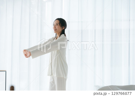 朝日を浴びながらストレッチをするパジャマの女性 129766877