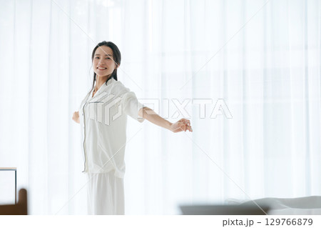 朝日を浴びながらストレッチをするパジャマの女性 朝日を浴びながらストレッチをするパジャマの女性 129766879