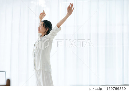 朝日を浴びながらストレッチをするパジャマの女性 129766880