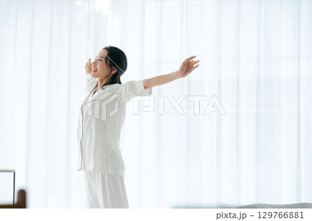 朝日を浴びながらストレッチをするパジャマの女性 129766881