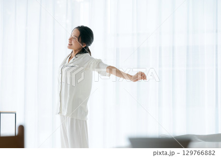 朝日を浴びながらストレッチをするパジャマの女性 129766882