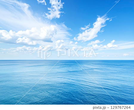 Blue waves reflect the summer sunlight, painting a serene seascape where the ocean meets the horizon under a vast, cloudy sky 129767264