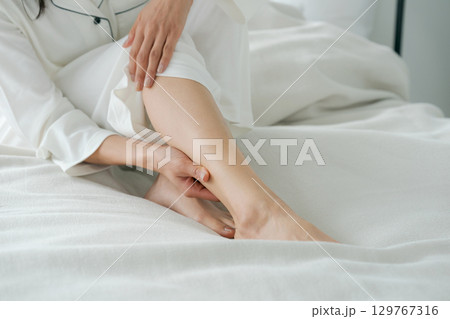 ベッドに座り足をマッサージする女性 129767316