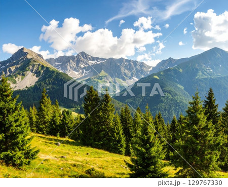 Alpine summer landscape with green valleys, snow-capped peaks, and a clear blue sky 129767330