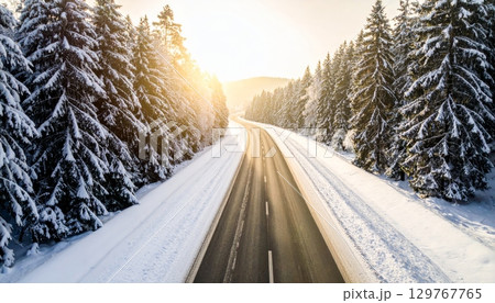 A car travels a snowy country road through a white forest landscape under a cold sky A car travels a snowy country road through a white forest landscape under a cold sky 129767765