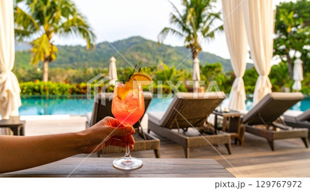 Sipping a refreshing tropical cocktail while relaxing in a chair by the beach, surrounded by a paradise of palm trees and the clear blue ocean Sipping a refreshing tropical cocktail while relaxing in a chair by the beach, surrounded by a paradise of palm trees and the clear blue ocean 129767972