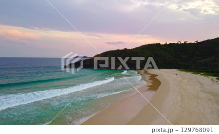 Vibrant summer sunset over the tropical coast with waves washing the sandy shore 129768091
