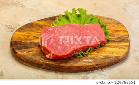 Freshly grilled raw beef steak on a wooden board with a side of vegetables, ready for a gourmet dinner 129768151