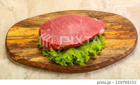 Freshly grilled raw beef steak on a wooden board with a side of vegetables, ready for a gourmet dinner Freshly grilled raw beef steak on a wooden board with a side of vegetables, ready for a gourmet dinner 129768152