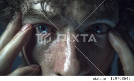 Man opening his eyes, revealing blue eyes with fingers 129768645