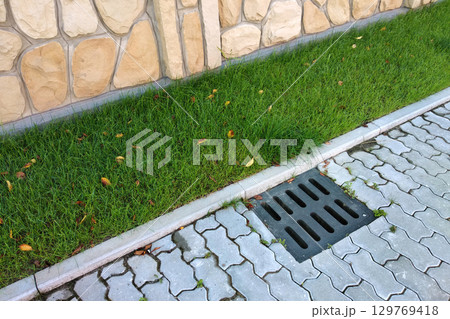 Plastic drain gutter, green grass lawn and stone pavement sidewalk. 129769418