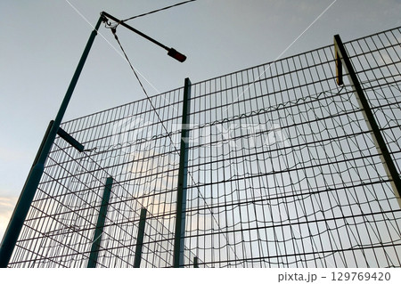 High wire mesh fence in restricted area on blue sky background. High wire mesh fence in restricted area on blue sky background. 129769420