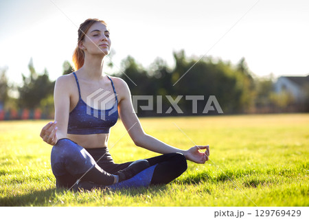 Young sportive woman in yoga position meditates in field at sunrise. Young sportive woman in yoga position meditates in field at sunrise. 129769429