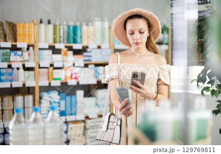 Girl in summer clothes scans code on package of cream to check expiration date 129769811