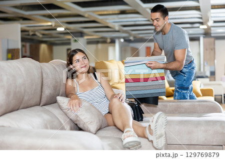 Woman is sitting on sofa and sales consultant shows her set of upholstery fabrics 129769879