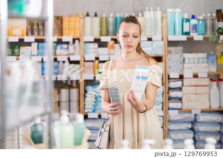Girl in summer clothes choosing skin cream at drugstore Girl in summer clothes choosing skin cream at drugstore 129769953