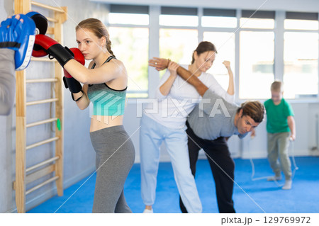 Focused teenager girl in boxing gloves practices punches with man in mitts in gym Focused teenager girl in boxing gloves practices punches with man in mitts in gym 129769972