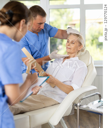 Man dermatologist examines skin of senior womans face, female nurse records data in client card Man dermatologist examines skin of senior womans face, female nurse records data in client card 129770124