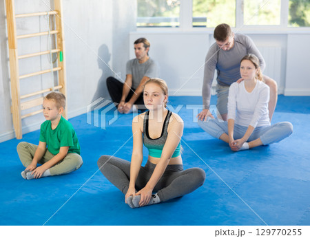Family during group workout with trainer in gym performs stretching of muscles of inner thigh by performing butterfly exercise Family during group workout with trainer in gym performs stretching of muscles of inner thigh by performing butterfly exercise 129770255