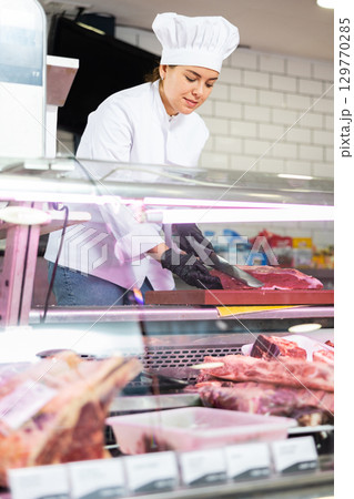 Female butcher slicing raw beef fillet for customer 129770285