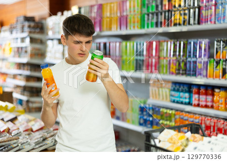 Thoughtful young guy choosing soft drinks in grocery store 129770336
