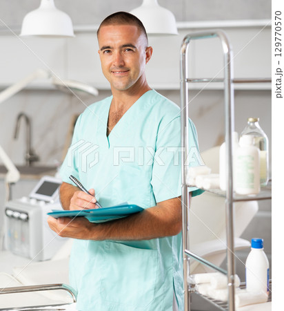 Portrait shot of male doctor holding clipboard in hand while standing in medical esthetic clinic 129770570