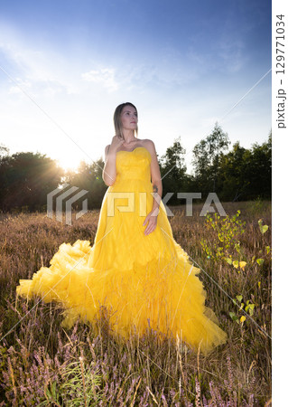 A Stunning Woman Wearing a Beautiful Yellow Dress Posed Gracefully Against a Vibrant Sunset 129771034