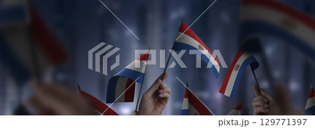 Paraguay flags in their hands on a blurred urban background 129771397