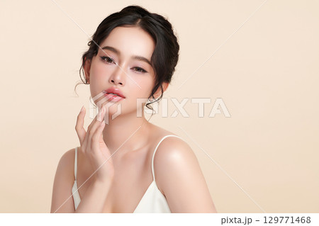 A beautiful young Asian woman with clean, fresh skin against a beige background. Skincare, facial treatment, cosmetology, beauty, and spa. An elegant portrait of an Asian woman. 129771468
