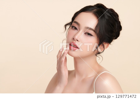A beautiful young Asian woman with clean, fresh skin against a beige background. Skincare, facial treatment, cosmetology, beauty, and spa. An elegant portrait of an Asian woman. 129771472