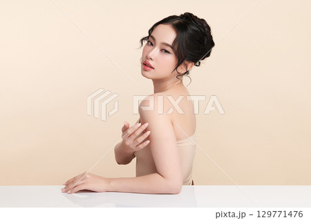 A beautiful young Asian woman with clean, fresh skin against a beige background. Skincare, facial treatment, cosmetology, beauty, and spa. An elegant portrait of an Asian woman. 129771476