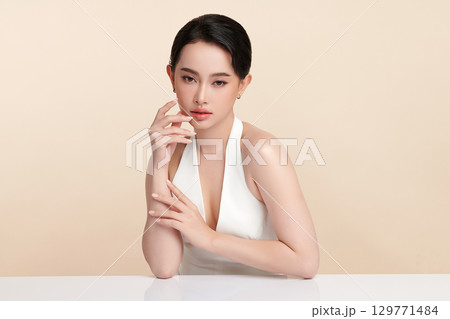A beautiful young Asian woman with clean, fresh skin against a beige background. Skincare, facial treatment, cosmetology, beauty, and spa. An elegant portrait of an Asian woman. 129771484