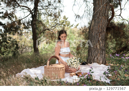 Picnic Woman Daisies: Young woman has picnic with daisies near tree to enjoy sunlight outdoor. 129771567