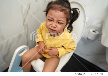 toddler girl sitting on toilet at home and suffering from stomachache and constipation toddler girl sitting on toilet at home and suffering from stomachache and constipation 129771910