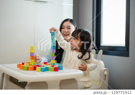 happy toddler girl playing wooden block toy cubes with her mother on table 129771912