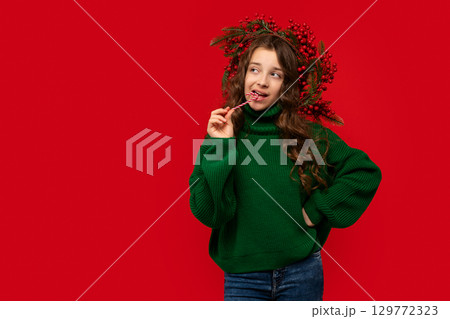 Young girl in green sweater biting a candy cane 129772323