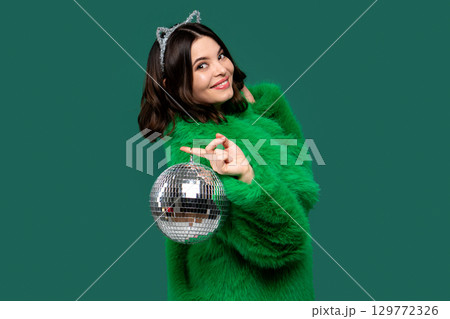 Elegant woman in green fur coat posing with disco ball. Elegant woman in green fur coat posing with disco ball. 129772326