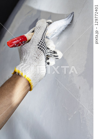 Construction worker in gloves using a paintbrush to apply paint to a wall during home renovation. Home renovation project Construction worker in gloves using a paintbrush to apply paint to a wall during home renovation. Home renovation project 129772401