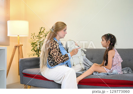 Little girl showing unwillingness to go to school as her mother holds a backpack 129773060