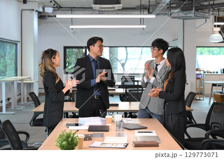 Group of business professionals congratulating a team member in a modern office Group of business professionals congratulating a team member in a modern office 129773071
