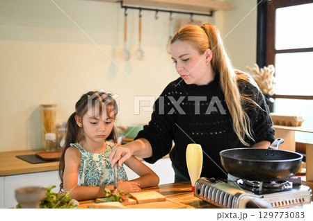 Family morning activity, mom teaching her daughter how to prepare breakfast in a home kitchen Family morning activity, mom teaching her daughter how to prepare breakfast in a home kitchen 129773083