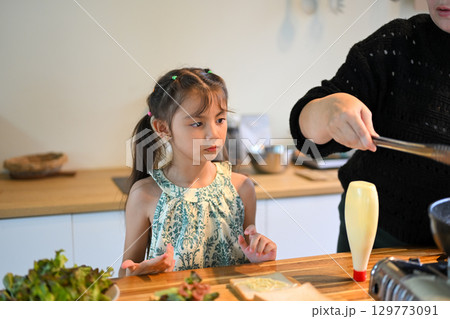 Little girl looking curious and attentive in the kitchen during meal making process 129773091