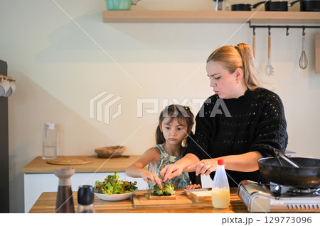 Young girl assisting her mom with breakfast preparation, learning cooking skills at home 129773096