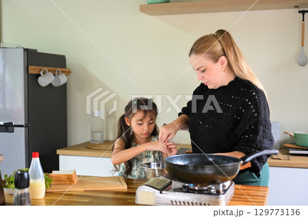 Mother and daughter preparing breakfast together in the kitchen 129773136