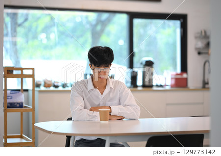 Thoughtful male employee sitting alone at a table with a paper coffee cup 129773142
