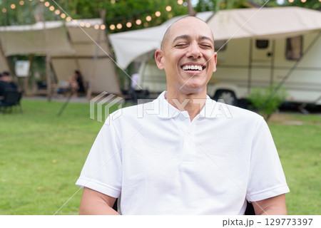 Confident bald man relaxing at campsite with camper van laughing with eyes closed 129773397